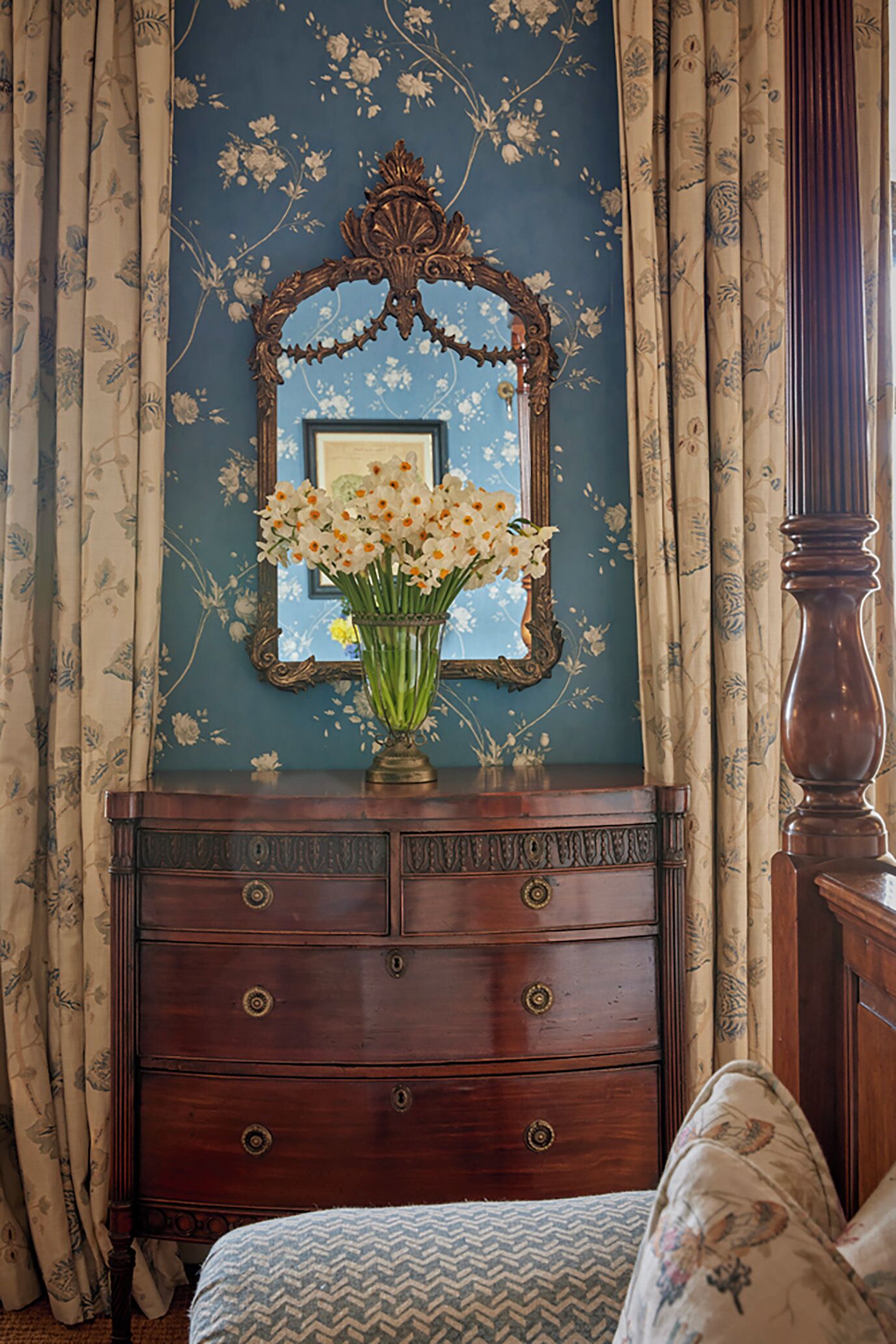 A bedroom with a dresser, a mirror, and a floral-patterned wall.