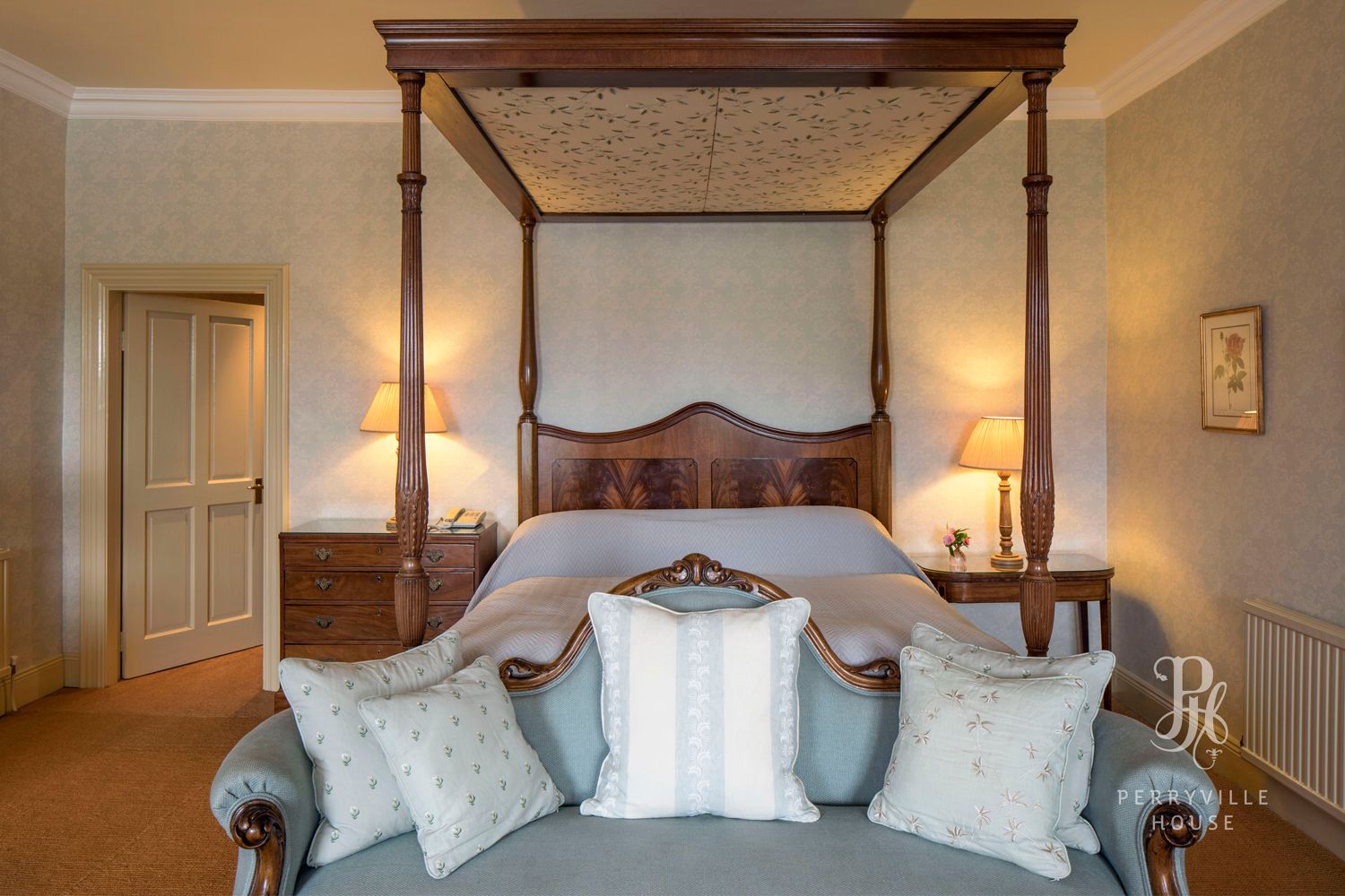 A four-poster bed with a wooden headboard, two bedside tables with lamps, and a floral-patterned wall.
