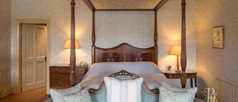 A four-poster bed with a wooden headboard, two bedside tables with lamps, and a floral-patterned wall.