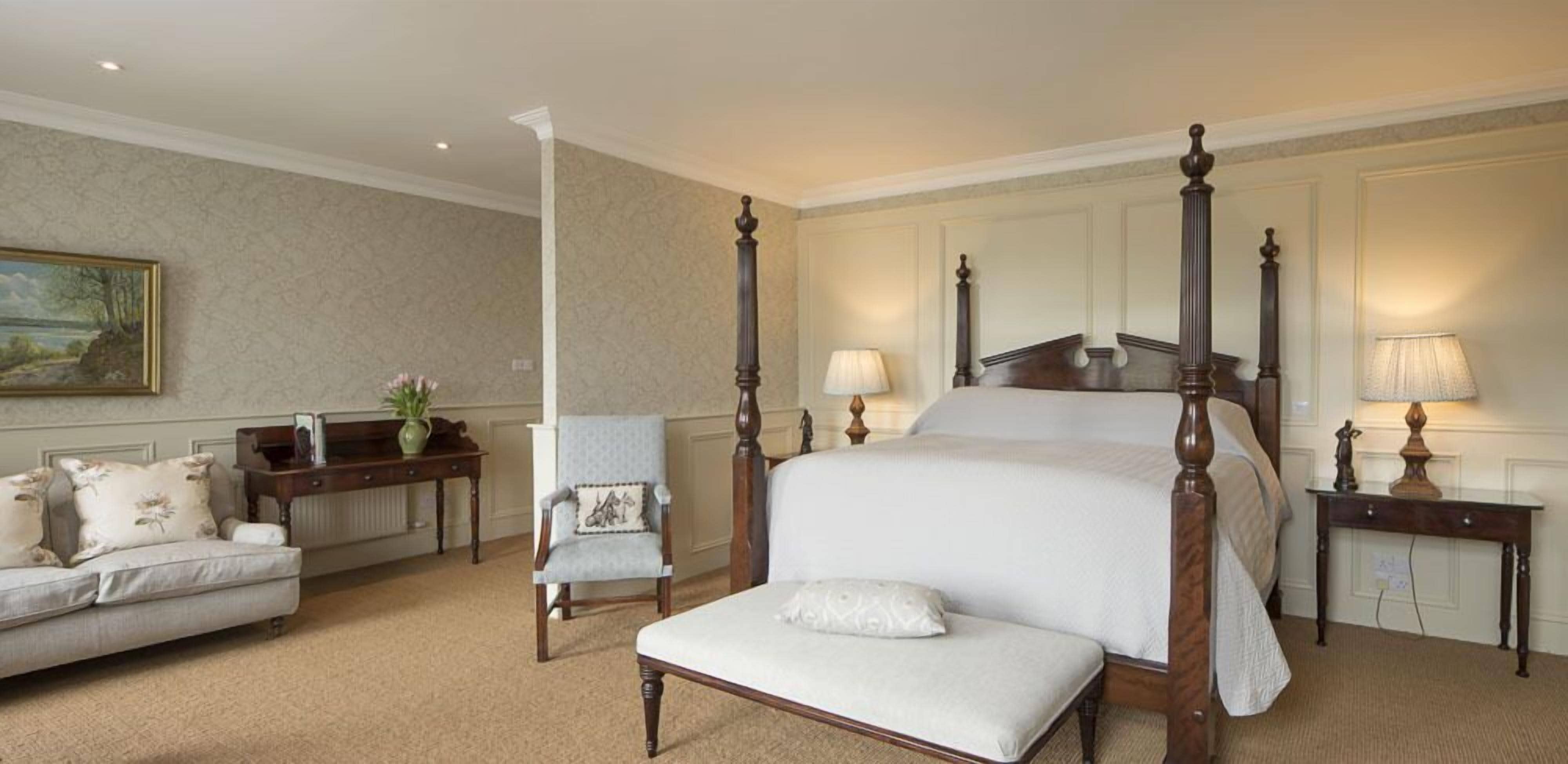 Um quarto espaçoso com cama de dossel, área de estar com sofá e poltrona, e mesa de cabeceira com luminárias.