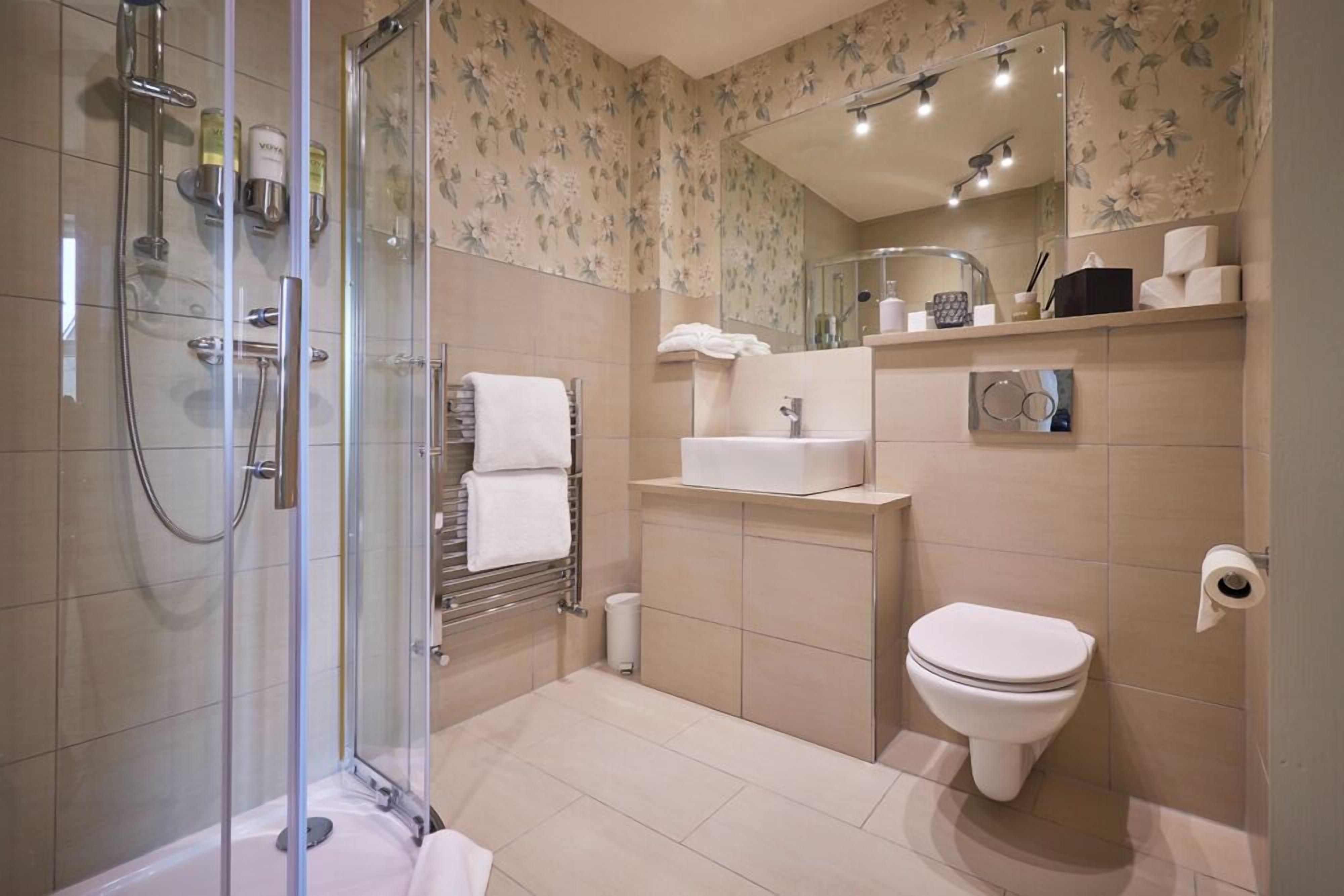 A modern bathroom with a glass-enclosed shower, a sink, a toilet, and a mirror.