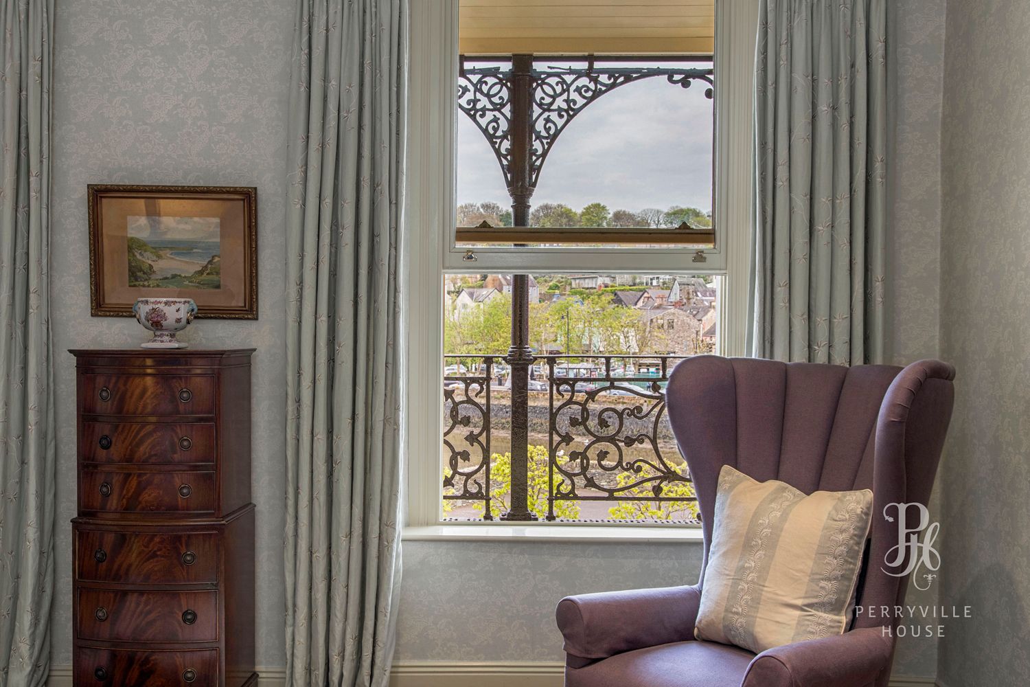 A room with a view of a balcony, a wooden dresser, and a purple armchair with a cushion.