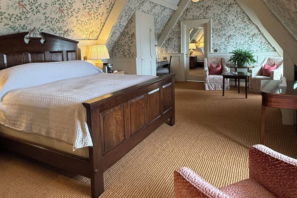 A bedroom with a wooden bed, a red chair, and a view of the living area through a door.