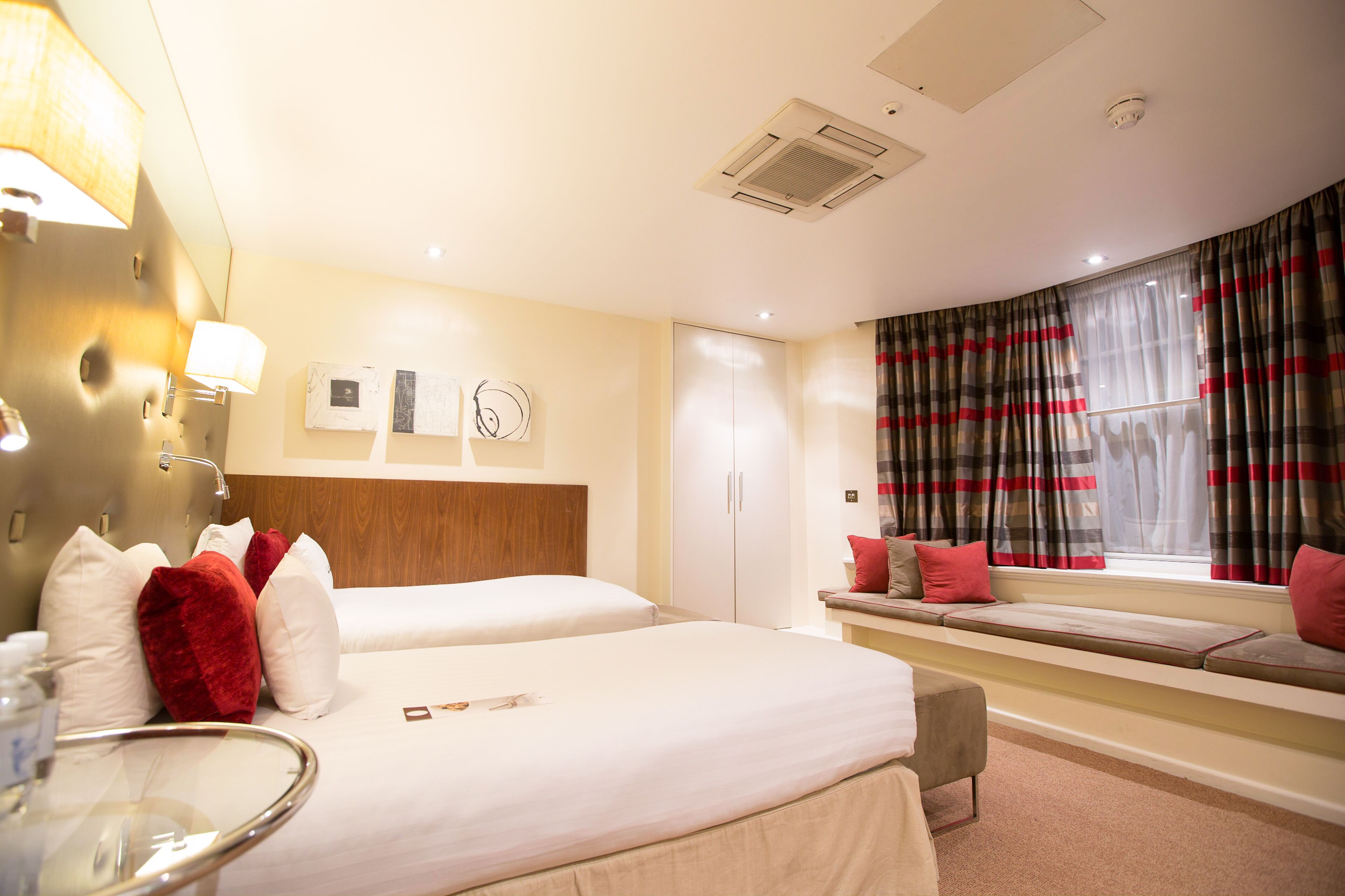 Habitación de hotel con dos camas, una zona de estar junto a la ventana y un baño con espejo y lavamanos.