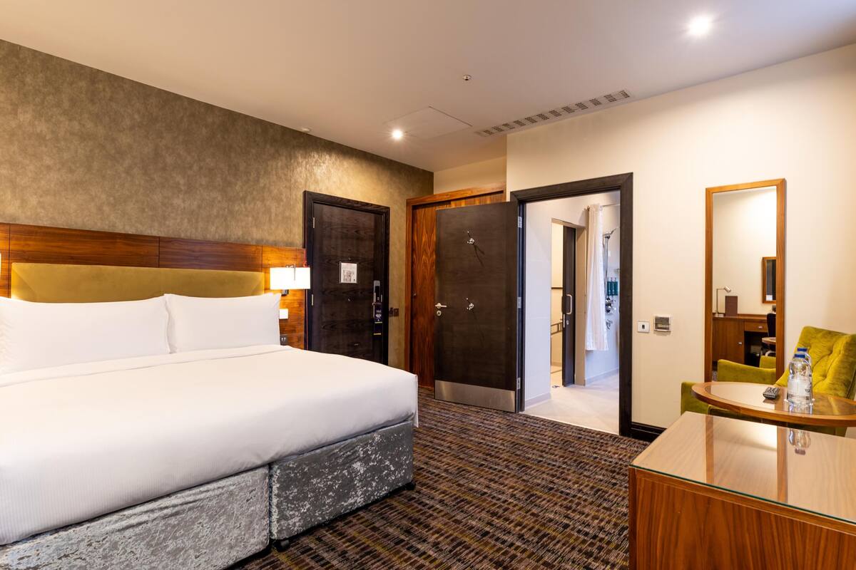 A hotel room with a bed, a desk, a chair, a mirror, and a door leading to a bathroom.