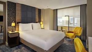 A hotel room with a large bed, bedside lamps, a small round table with a lamp, a yellow chair, and a window with curtains. - DoubleTree by Hilton London West End (London)