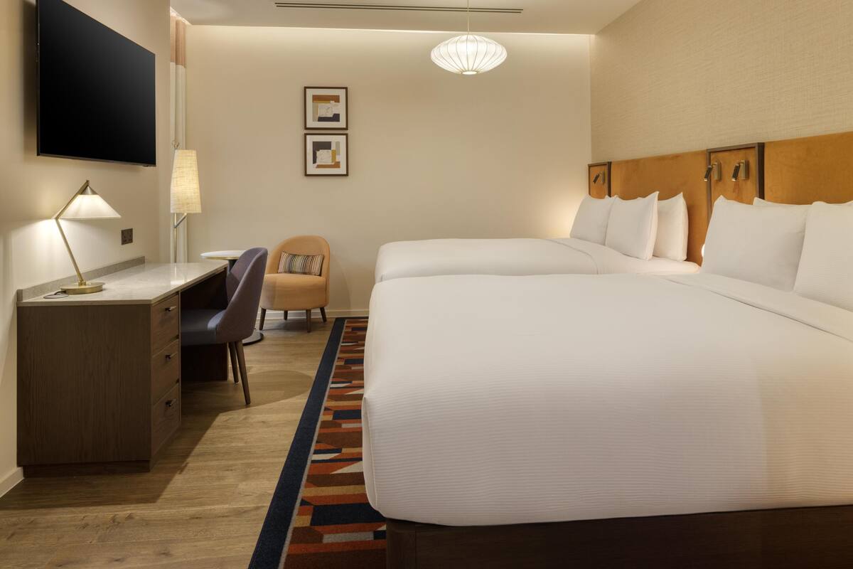 A hotel room with a large bed, a desk with a lamp, a chair, and a TV mounted on the wall.