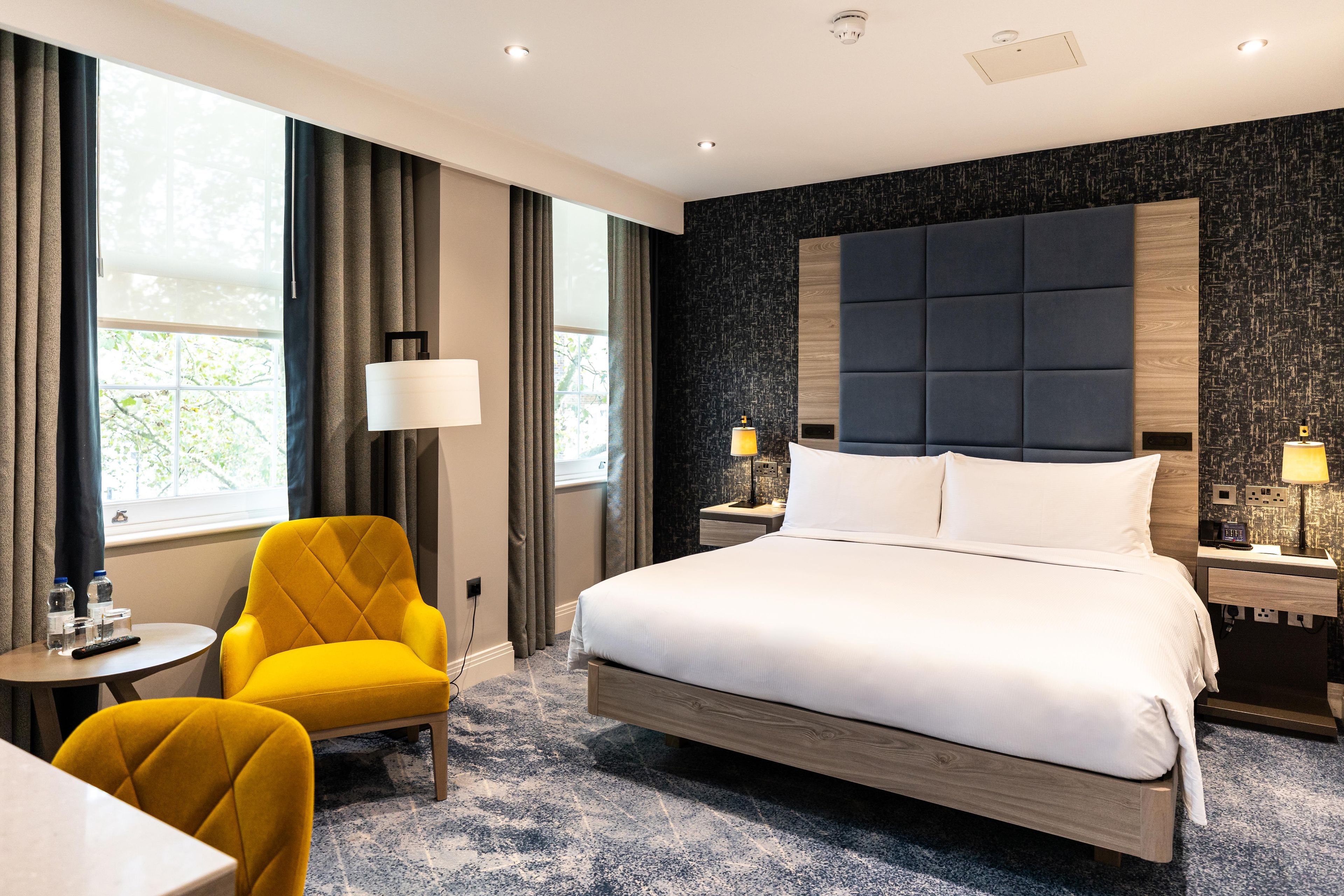 Une chambre d’hôtel avec un grand lit, une table de chevet, une chaise et une vue sur l’extérieur par la fenêtre.