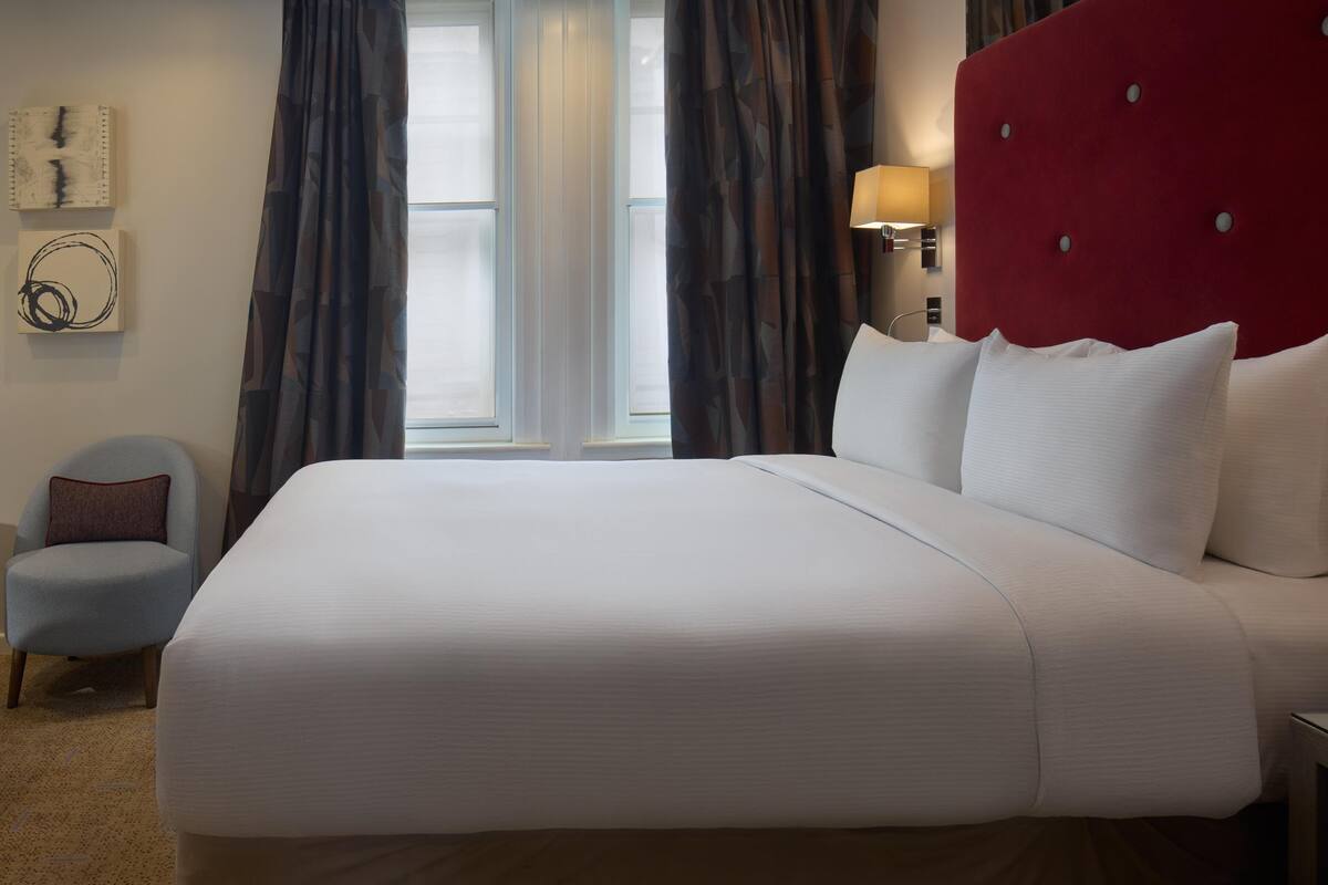 A large bed with white linens, a red headboard, and a wall-mounted lamp.