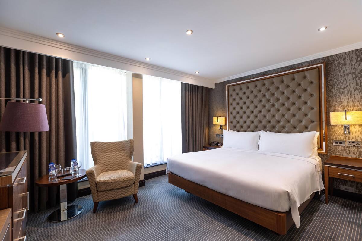 A hotel room with a large bed, a chair, a desk, and a lamp.