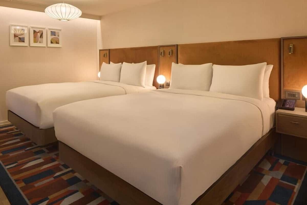 A hotel room with two beds, a patterned carpet, and a wall-mounted light fixture.