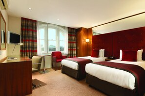 A hotel room with two beds, a desk, a chair, a TV, and a window with curtains. - DoubleTree by Hilton London West End (London)