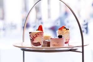 A dessert trolley with various desserts, including a strawberry-topped dessert and a chocolate dessert, on a metal stand.