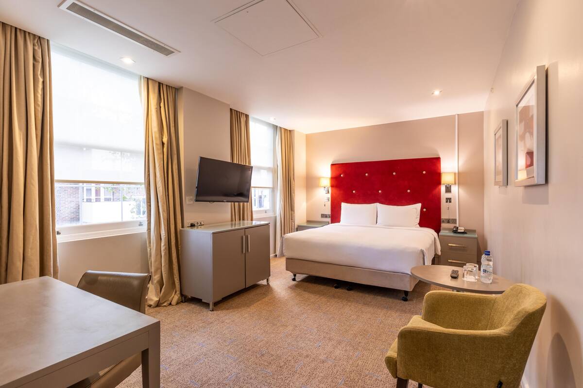 A hotel room with a bed, a desk, a chair, a TV, and a window with curtains.