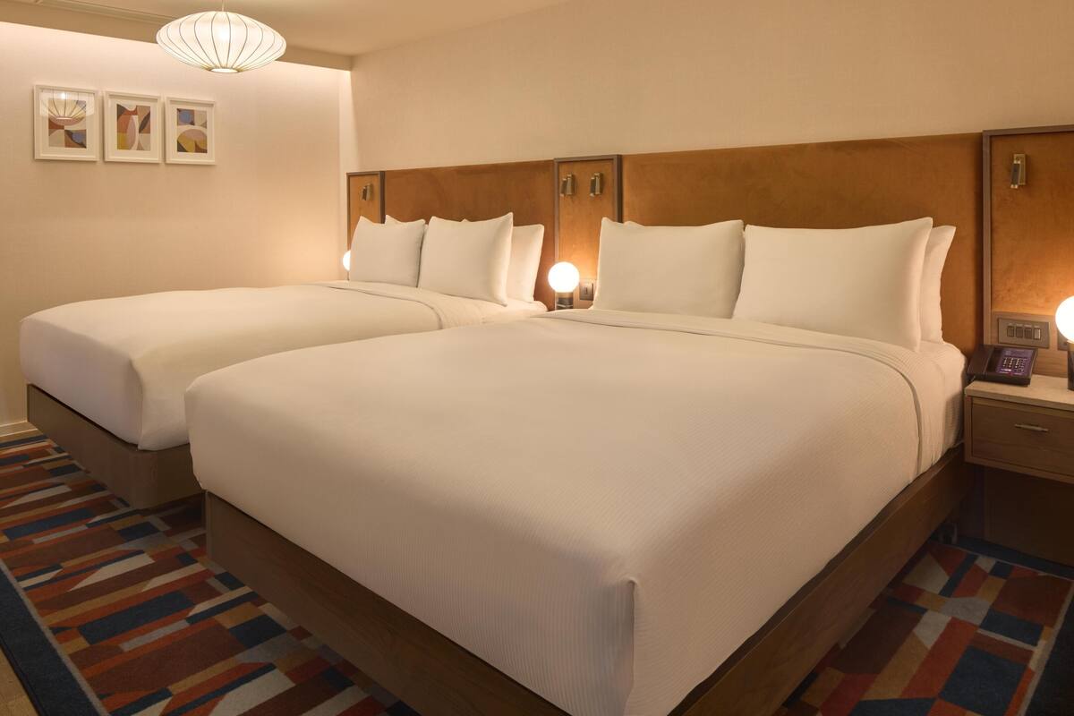 A hotel room with two beds, a wooden headboard, a nightstand with a phone, and a patterned rug.