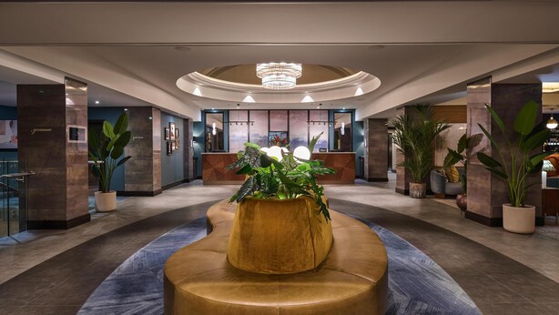 A lobby with a central seating area, a reception desk, and potted plants. - DoubleTree by Hilton London West End (London)