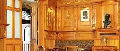 Un intérieur en bois agrémenté d’un lustre, d’un buste posé sur un piédestal et d’une pancarte sur laquelle on peut lire : « L’IRLANDE EST UNIQUE EN SON GENRE ».