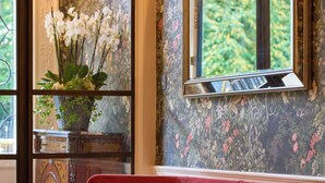 Un banco rojo en una habitación con papel tapiz floral, un espejo y una ventana que da a vistas de vegetación.