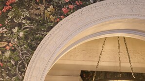 Una gran escalera con un fondo de papel tapiz floral, un columnario blanco ornamentado y un candelabro de cristal.