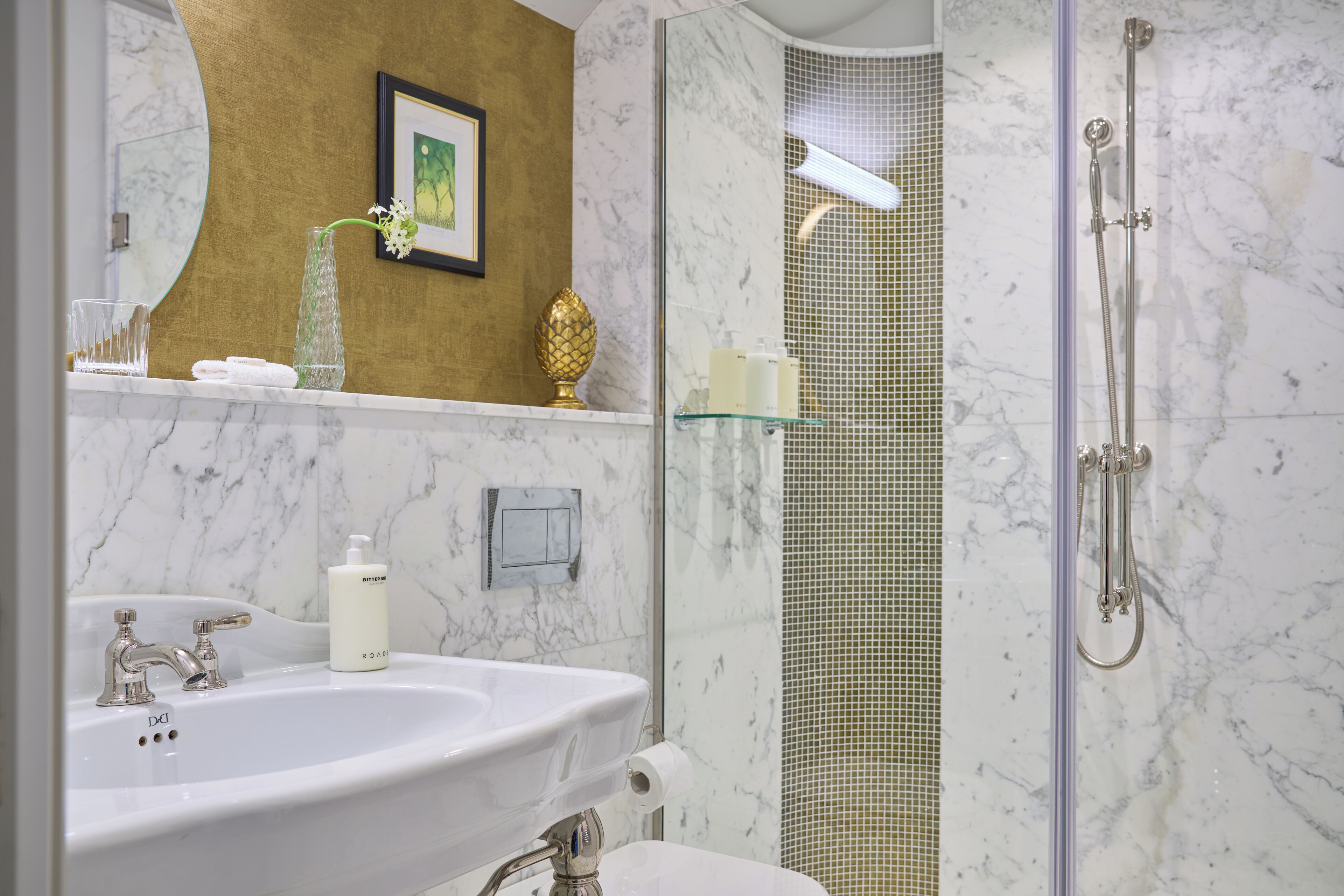 Um banheiro com pia de mármore, chuveiro com porta de vidro e parede cor de dourado.