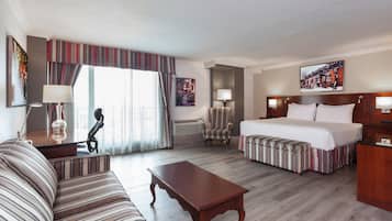 Quarto de hotel com cama, sofá, poltrona, escrivaninha e luminária.
