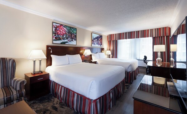 A hotel room with two beds, a desk, a chair, a TV, and a painting on the wall.