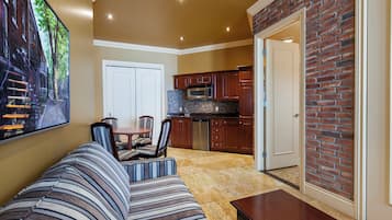 A living room with a striped sofa, a dining table, and chairs. There is a kitchen area with wooden cabinets and a microwave.