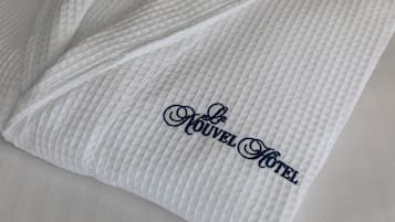 A white textured pillow with embroidered text "Nouveau Hotel".
