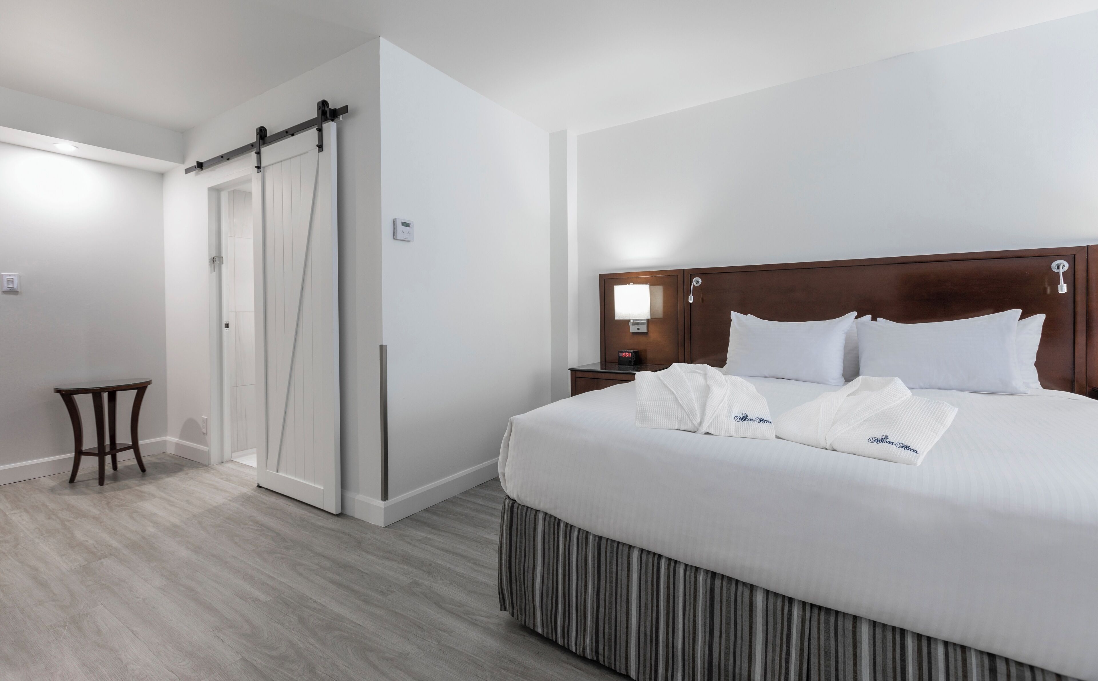 Habitación de hotel con una cama grande, cabecera de madera, mesita de noche, una pequeña mesa y una puerta corrediza.