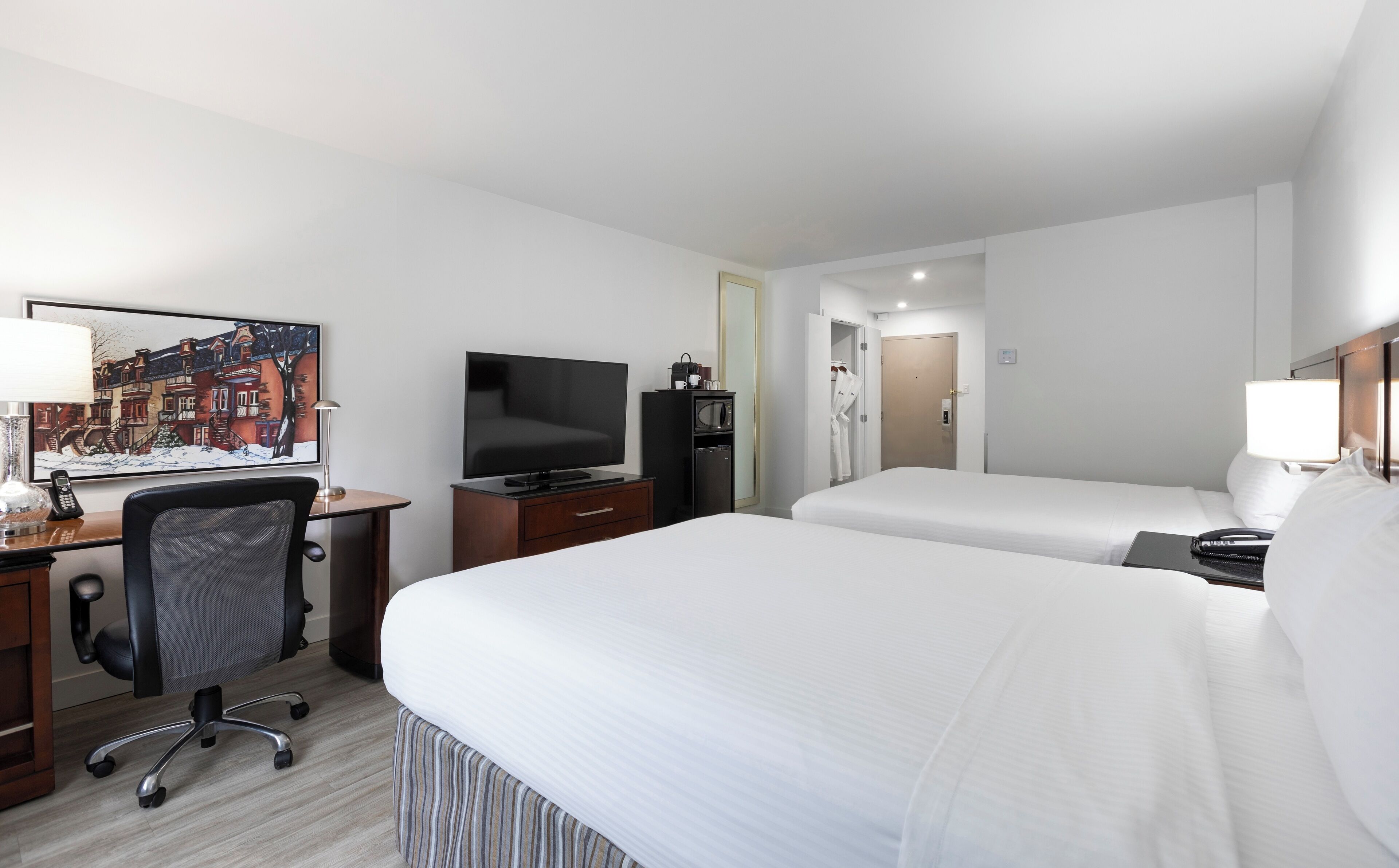 Ein Hotelzimmer mit einem Bett, einem Schreibtisch mit Computer, einem Fernseher und einem Bild an der Wand.