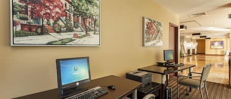 Habitación de hotel con escritorio, computadora, impresora y una silla. Dos cuadros grandes adornan la pared.