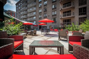 An outdoor patio area with wicker furniture, red cushions, and tables. - Le Nouvel Hotel (Montreal)