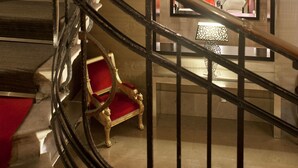 A grand staircase with a curved railing leading to a room with a chandelier and red upholstered chairs. - Savoy Hotel (Buenos Aires)