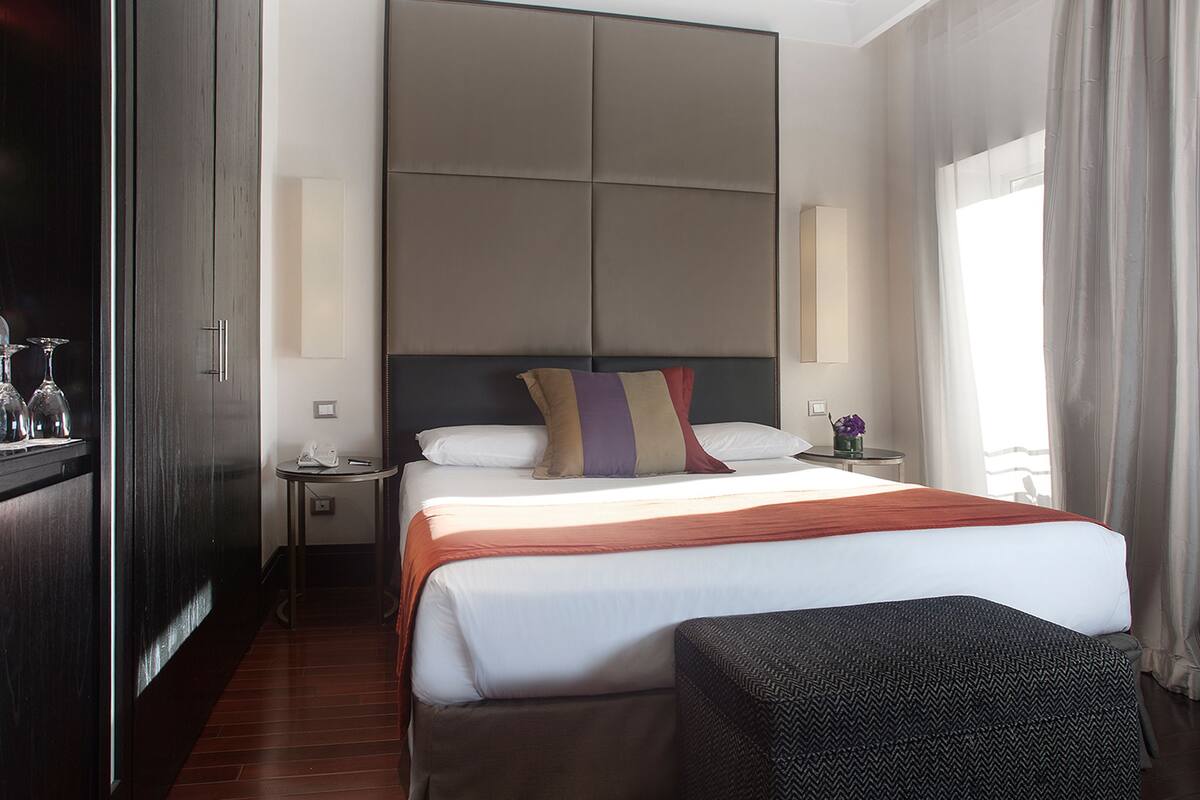 Habitación de hotel con una cama grande, una mesita de noche, un armario y una silla.