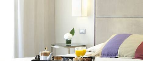 Una habitación de hotel con una cama, una bandeja con artículos de desayuno, un florero con una flor y una lámpara fijada a la pared.