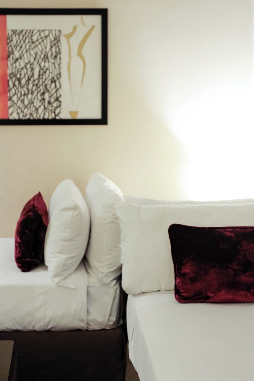 A hotel room with a bed, white bedding, and a red and black pillow.