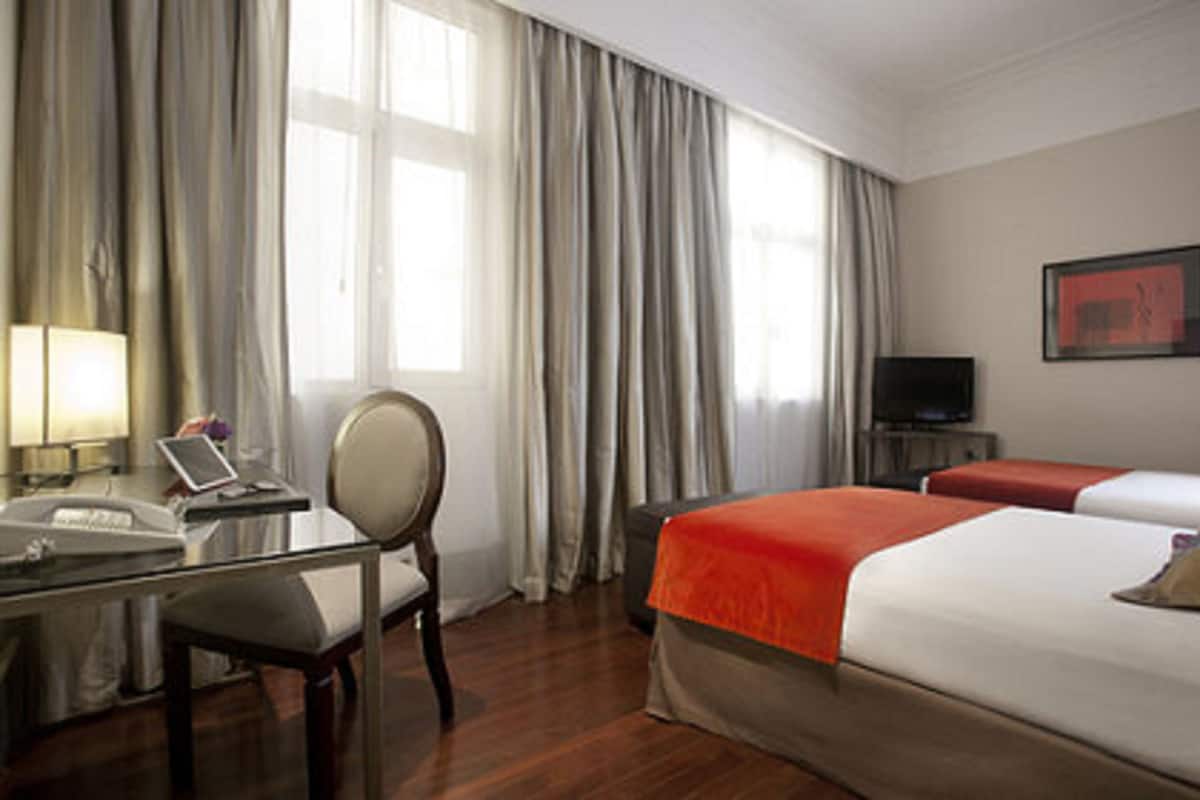 Habitación de hotel con escritorio, silla, dos camas, televisor y ventana con cortinas.