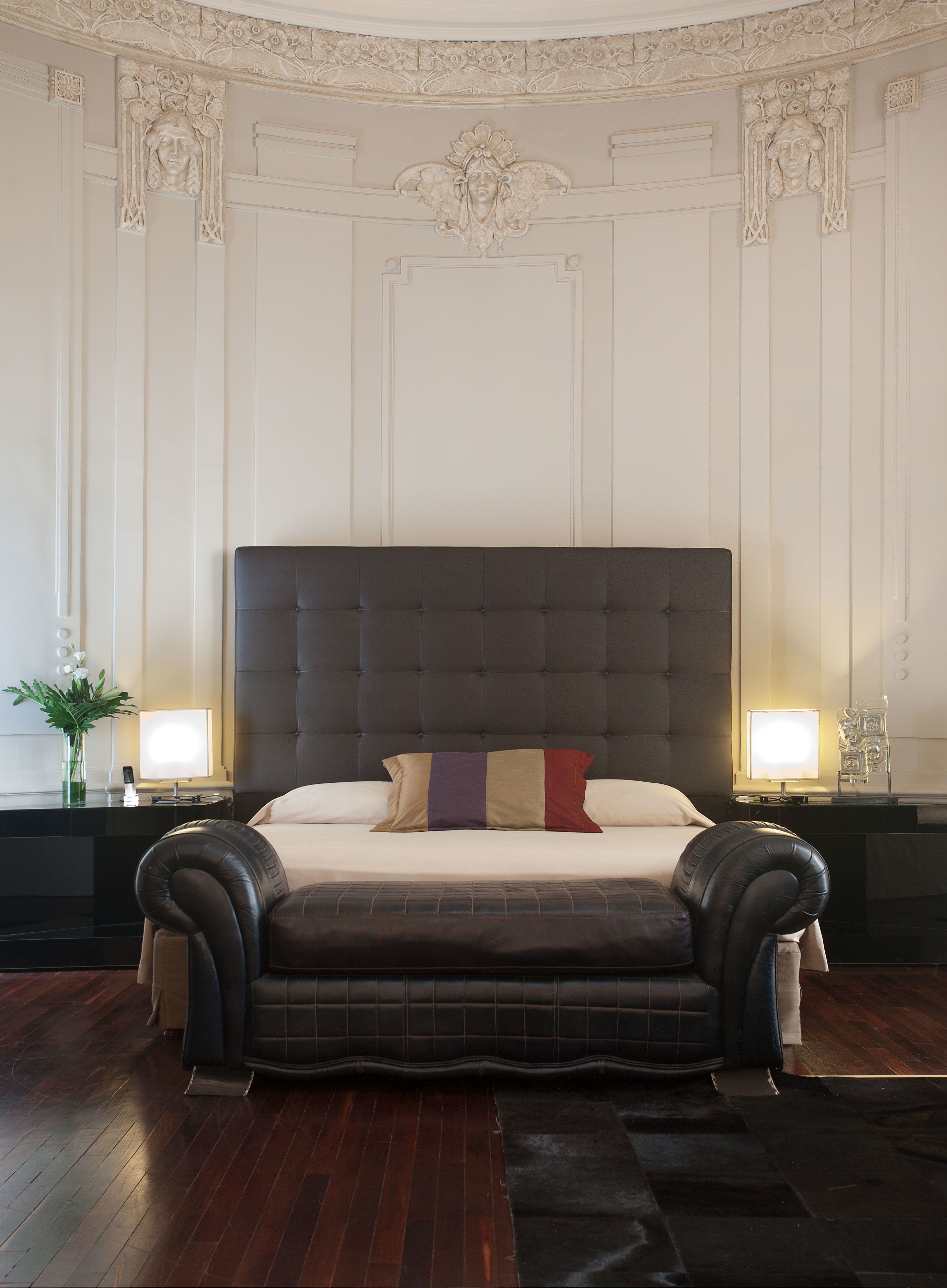 A large, dark-toned bed with a tufted headboard in a room with ornate wall decorations and a wooden floor.