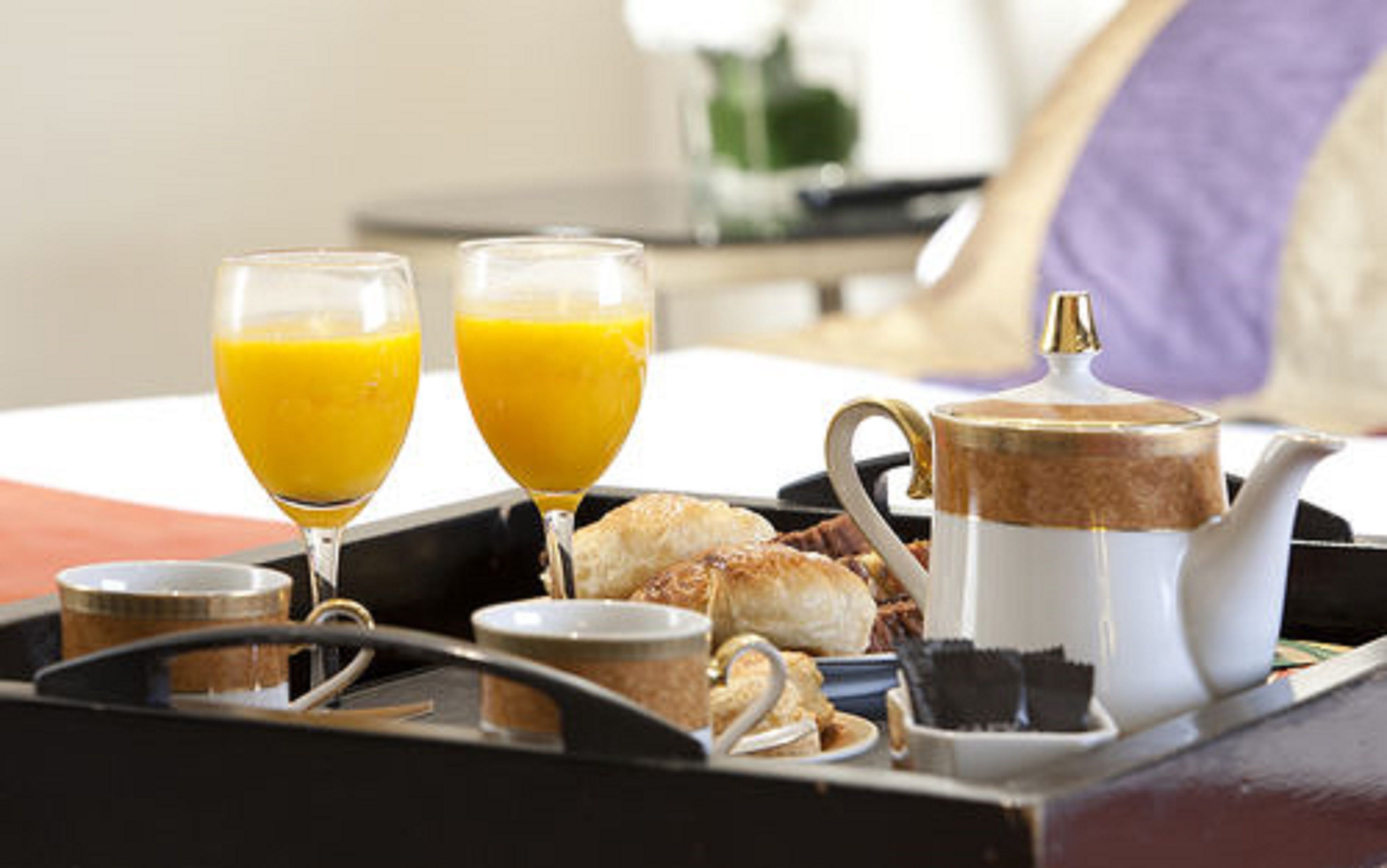 Una bandeja de desayuno con dos vasos de zumo de naranja, una tetera, una taza y bollería.
