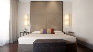 Una habitación de hotel moderna con una cama grande, dos mesitas de noche, un banco y un amplio ventanal con cortinas.