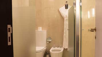 A modern bathroom with a glass shower enclosure, a toilet, bidet, and a towel hanging on the wall.