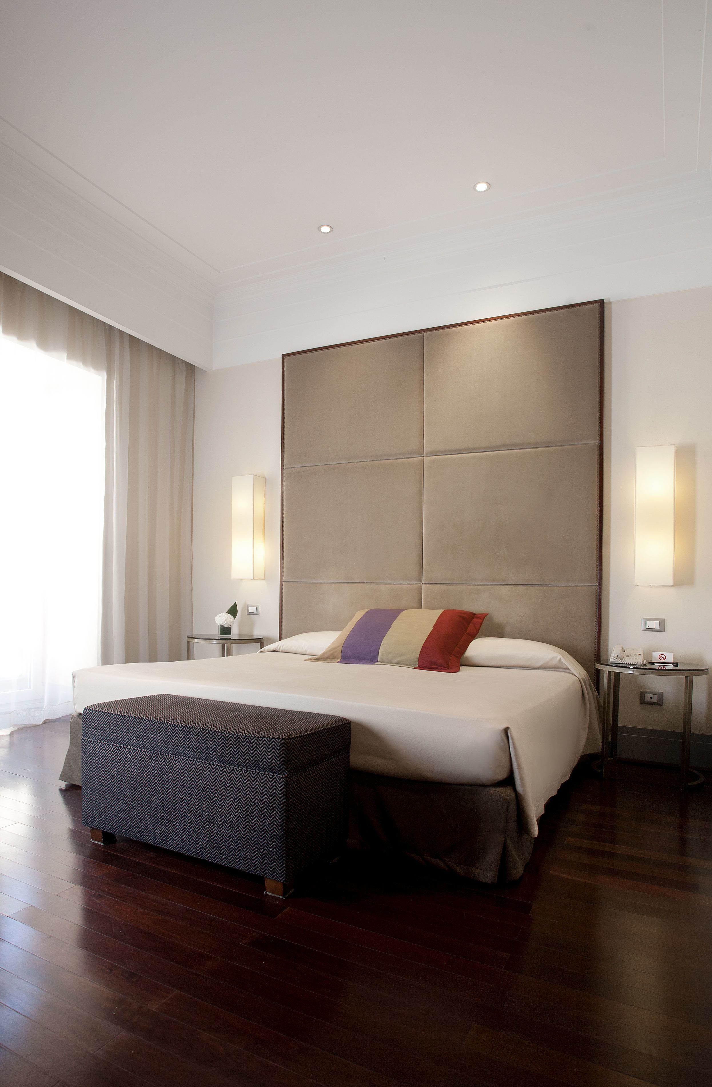 Een moderne hotelkamer met een groot bed, een nachtkastje, gordijnen voor een groot raam, en een wandlamp.