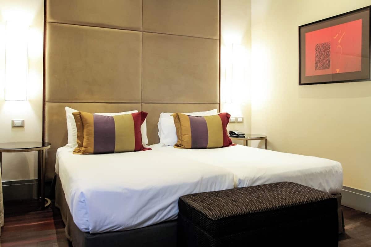 Una habitación de hotel con una cama grande, dos mesitas de noche, un banco y una obra de arte enmarcada en la pared.