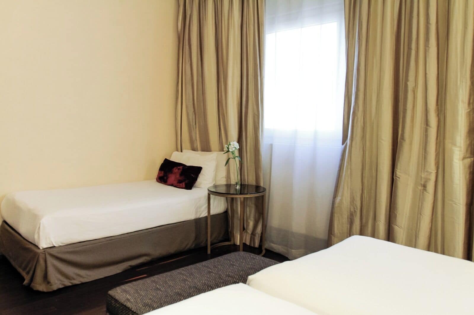 Quarto de hotel com duas camas, uma mesinha redonda e uma janela com cortinas.