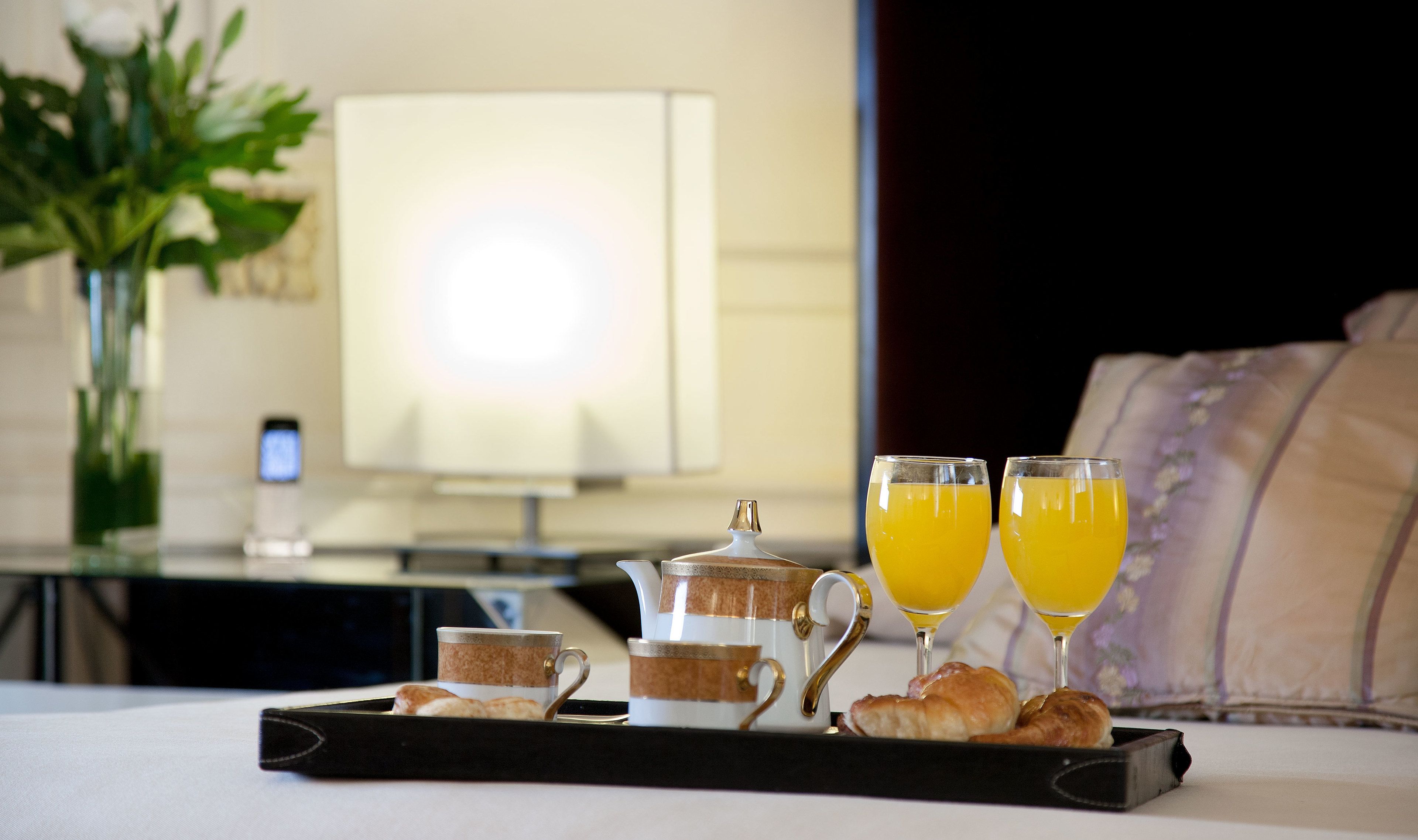 Bandeja de desayuno con cruasanes, un tetera y dos vasos de jugo de naranja sobre una cama.