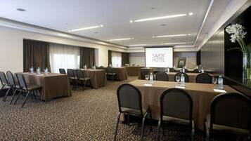 A conference room with a large screen, multiple tables with chairs, and a carpeted floor.