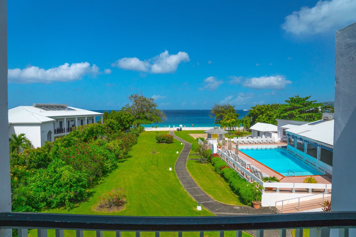 A resort with a swimming pool, a well-maintained lawn, and a view of the ocean.