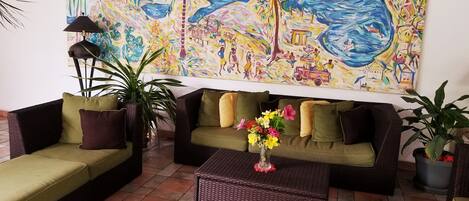 Una sala de estar con un mural grande y colorido, muebles de mimbre y una planta en maceta.