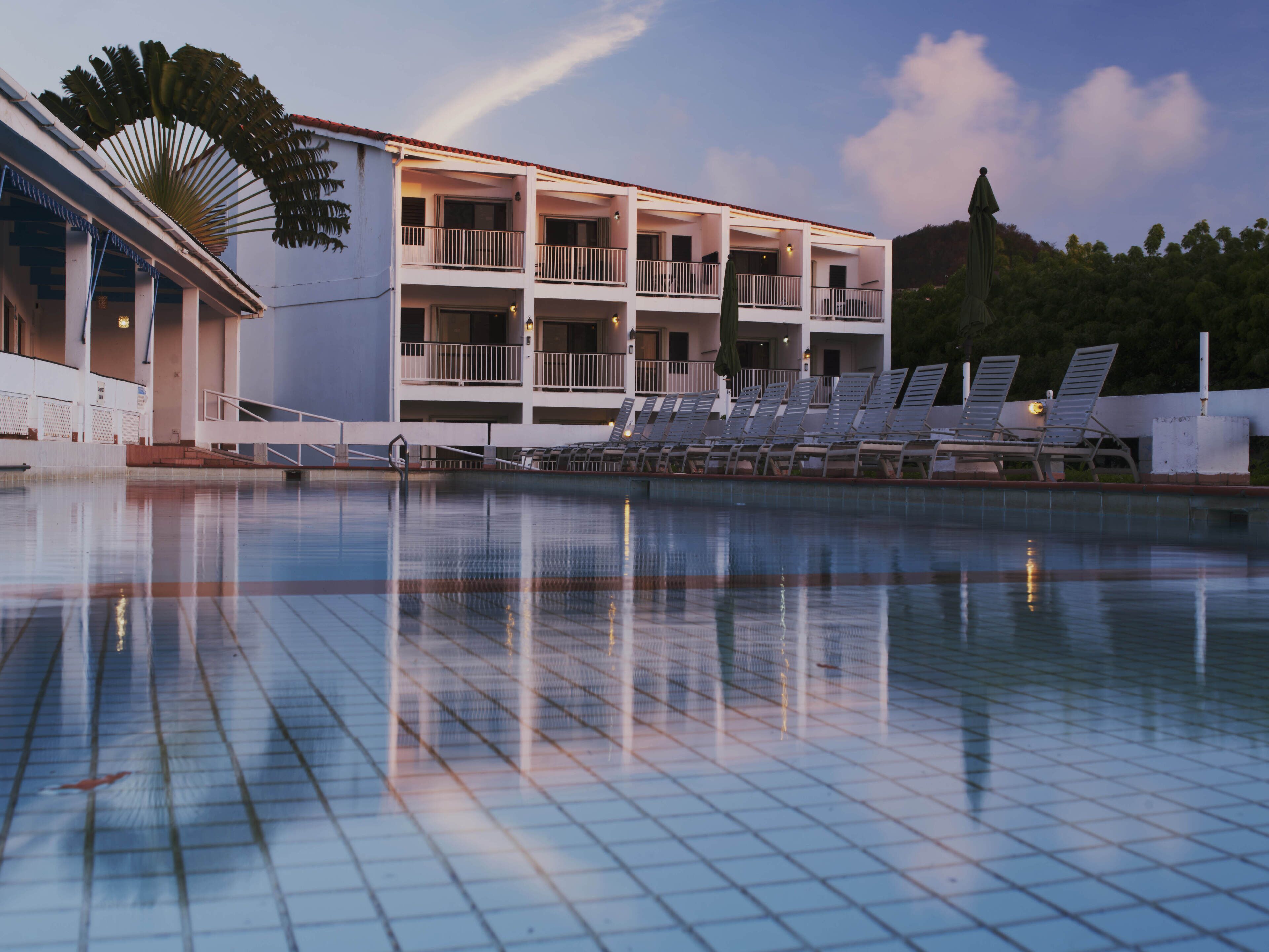 A swimming pool with lounge chairs and a building with multiple balconies.