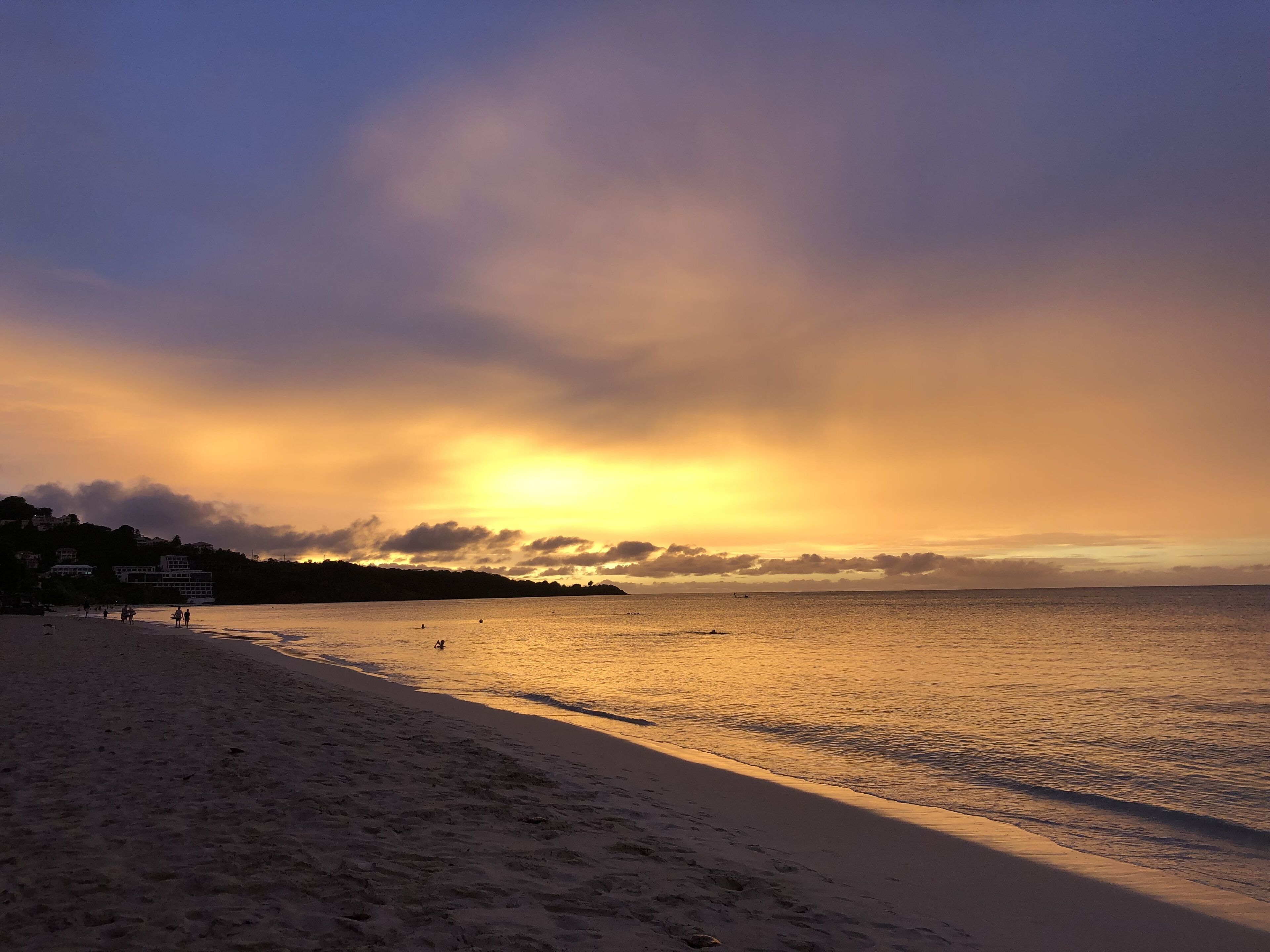 A beach with a clear sky and calm sea at sunset.